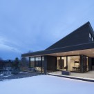 Casă cu volume din sticlă așezată pe panta unui deal înzăpezit din Quebec